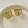 Elegant gold-finished feather-shaped stud earrings displayed on a white ceramic tray - Gold Feather Shape