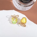 Close-up of golden bow and tulip earrings with yellow crystals on a white pedestal - Yellow Green/Tulip Shape