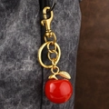 Porte-clés pomme rouge en résine avec attaches dorées sur un sac à main gris - Feuille d'or Pomme Rouge