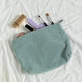 Makroaufnahme der mintgrünen Cord-Kosmetiktasche mit Make-up auf weißem Leinentuch - Hellgrün