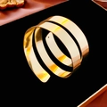 Detailed close-up of a wide spiral multi-layer golden bangle on a plush black display - Gold