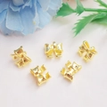 Cinco colgantes de lazo dorado para joyería DIY sobre tela rosa con detalle floral - Lazo con Retención de Color / Oro de 18K