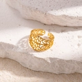 Eleganter vergoldeter Edelstahlring mit Hohlmuster, verstellbar auf weißem Steinboden - Hohlmuster / Gold