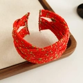 Gedetailleerd beeld van rode en gouden gelaagde kralenarmband op houten plateau - Rood