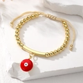 Detail of bohemian gold beaded bracelet with red evil eye charm on white stone base - Red Pendant