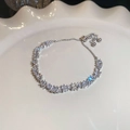 Detalle macro de pulsera plateada con circonitas y perlas en un plato blanco texturizado - Estilo Perla Circonita / Plateado