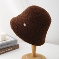 Detailed texture of brown fleece bucket hat with a gold metal plate on a wooden stand - Brown