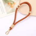 Detail of brown PU leather wristlet strap with gold rings and swivel clasp on ceramic tray - Brown