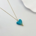 Elegant gold necklace with green heart pendant and drop metal detail on white background - Cyan