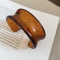 Detailed view of the wide amber resin cuff bracelet with marble texture on an open book - Quicksand Amber (Brown-Ink Round Open)
