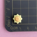 Close-up of small yellow resin sun charm with orange smiley face on a measuring mat - Sun Face