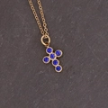 Macro shot of gold cross pendant with six inlaid blue gemstones on a stone surface - Royal Blue Cross Shape