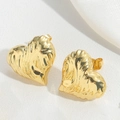 Primo piano di orecchini dorati a forma di cuore su elegante superficie bianca - Stile Cuore