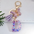 Detail of purple letter D keychain with glitter resin, suede tassel and golden butterfly - Letter D