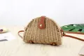Detail view of semi-circular straw crossbody bag with brown leather base and rivets - Tan