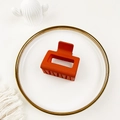 Top view of matte orange rectangular hair claw clip on a decorative gold-rimmed white plate - Orange