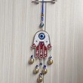 Detail of red Hamsa hand wall hanging with blue evil eyes and small brass bells decoration - Red