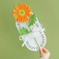 Handmade orange knitted daisy flower tied with a ribbon on white oval card - Gerbera - Orange