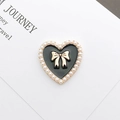 Detail of a vintage black heart charm with a golden bow and pearl edges on a white card - Enamel Pearl Heart / Black