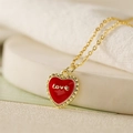 Detailopname van een gouden ketting met rode hart hanger en Love gravure op de voorkant - Hart-Love