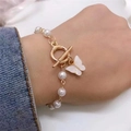 Vista macro de una pulsera de perlas con colgante de mariposa blanca y cierre de T dorado - Pulsera de Mariposa / Dorado