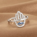Unique silver Hamsa hand ring featuring blue Evil Eye zircon stones on brown fabric - Hamsa Hand Style (Q-J089) / White Gold