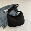 Quilted black puffer crossbody tote bag with knotted strap on a denim jacket background - Black