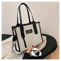 Close-up of beige canvas tote with black leather trim held by a model in a minimalist room - Black Small