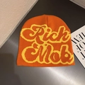 Detailed view of orange knitted beanie featuring bold Rich Mob yellow lettering and texture - Orange