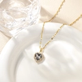 Detail of a heart-shaped gold necklace with dark gemstone and crystals on ceramic - Gray Pendant Necklace