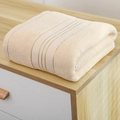 Thick light beige cotton bath towel with parallel jacquard lines on a wooden surface - 140x70cm / Beige