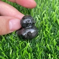 Macro detail of a polished natural dark stone duck figurine held over green grass - Larvikite