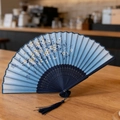 Blue gradient silk folding fan with white cherry blossom patterns and dark blue tassel - Blue Sakura Gradient