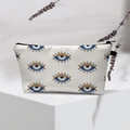 Close-up of cream evil eye makeup bag with black zipper on a white geometric platform - 32-Off-White Regular Eyes