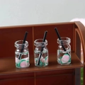 Miniature transparent beverage bottles with pink petals and black straw on brown stand - Fruit Cup 4