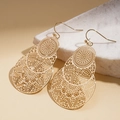 Macro view of gold hollow metal earrings with intricate floral and geometric details - Gold