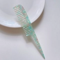 Detailed view of pale green marble texture acetate tail comb with wide teeth on white plate - Cyan