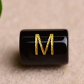 Macro shot of black agate bead with gold letter M engraving for DIY jewelry - M