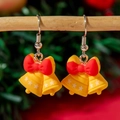 Gros plan de boucles d'oreilles cloches de Noël jaunes avec des nœuds rouges - Cloche de Noël