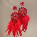 Dettaglio di orecchini con cristalli rossi e lunghe nappe di piume morbide su supporto - Rosso