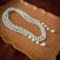 Macro detail of multi-layer pearl necklace with teardrop pendants and golden clasp - White