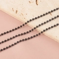 Vue détaillée de trois chaînes à billes en métal noir sur une pierre décorative - Chaîne Noire 2.4MM (1m)