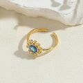 Nahaufnahme vom goldenen Sonnenblumenring mit blauem Evil Eye und funkelnden Kristallen - Blütenblatt-Stil (JZ0409)