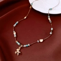 Detail shot of a beaded necklace with a gold bear pendant on luxury silk fabric - Puppy Pendant Beaded Style / Gold-Blue