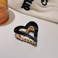 Macro detail of black heart-shaped acetate hair claw clip with golden metal spring - Black