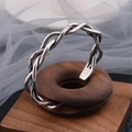 Vintage Thai silver twisted braid open bangle on wooden display stand with soft backdrop - Silver