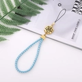 Blue braided phone strap with gold camellia charm on a lifestyle background - Blue