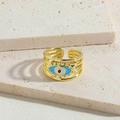 Detailed macro view of gold-plated evil eye ring on textured beige stone surface - Blue Enamel Ring