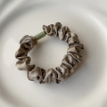 Detailed texture of champagne satin scrunchie with green cylindrical bead accent - Camel
