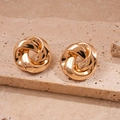 Nahaufnahme goldener geometrischer Knoten-Ohrstecker auf einer strukturierten Steinfläche - Gold